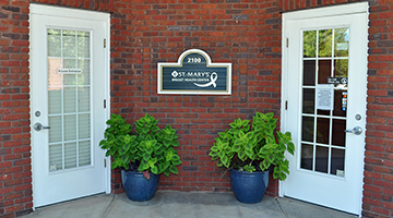 Two doors outside of a brick building with an address plate and two potted plants in between them